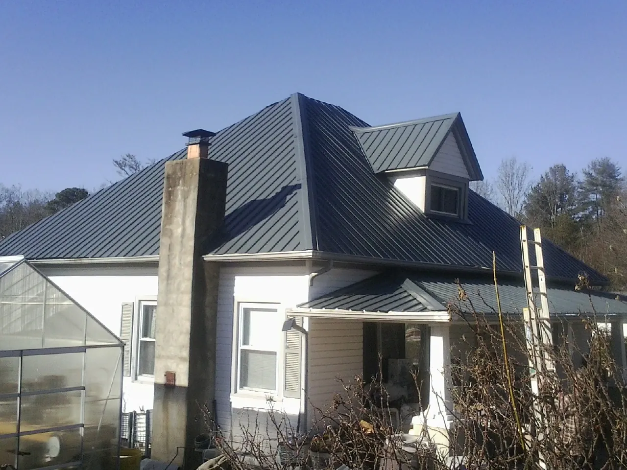 Dark blue standing seam metal roof on a white farmhouse with dormer — Slate & Tile Roof Repair by Roofing Brothers in Trego
