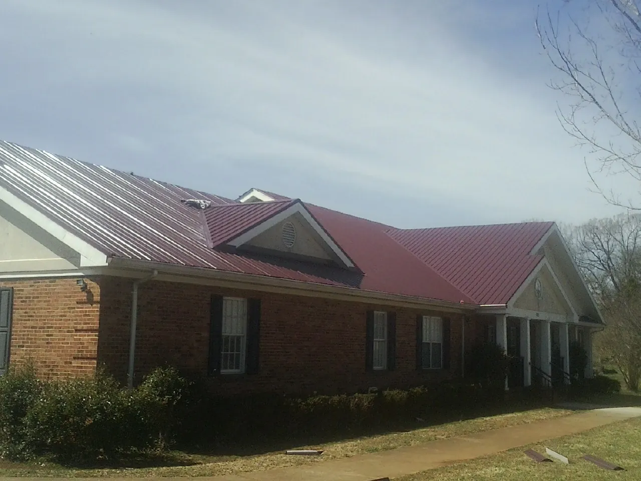 Red metal roof with gabled entries on a long brick building, from a Hail Damage Roof Repair job in Trego