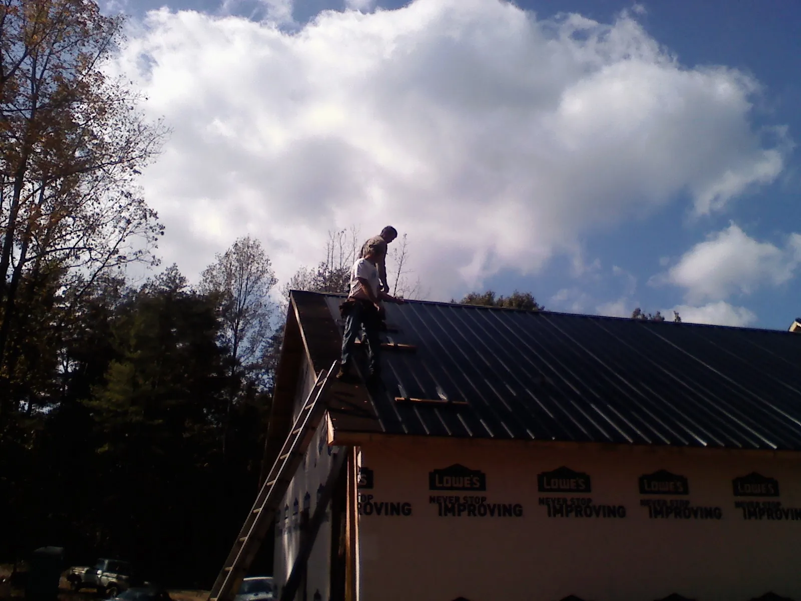 Roofer fastening dark metal panels high against a cloudy sky, from a Roof Inspection job in Trego