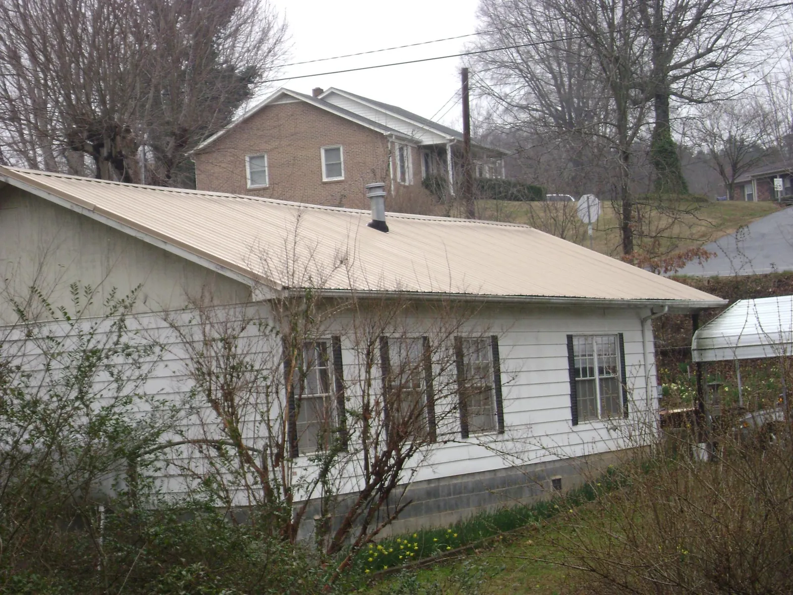 Tan metal roof on a white sided house set into a hillside — Commercial Roofing by Roofing Brothers in Trego
