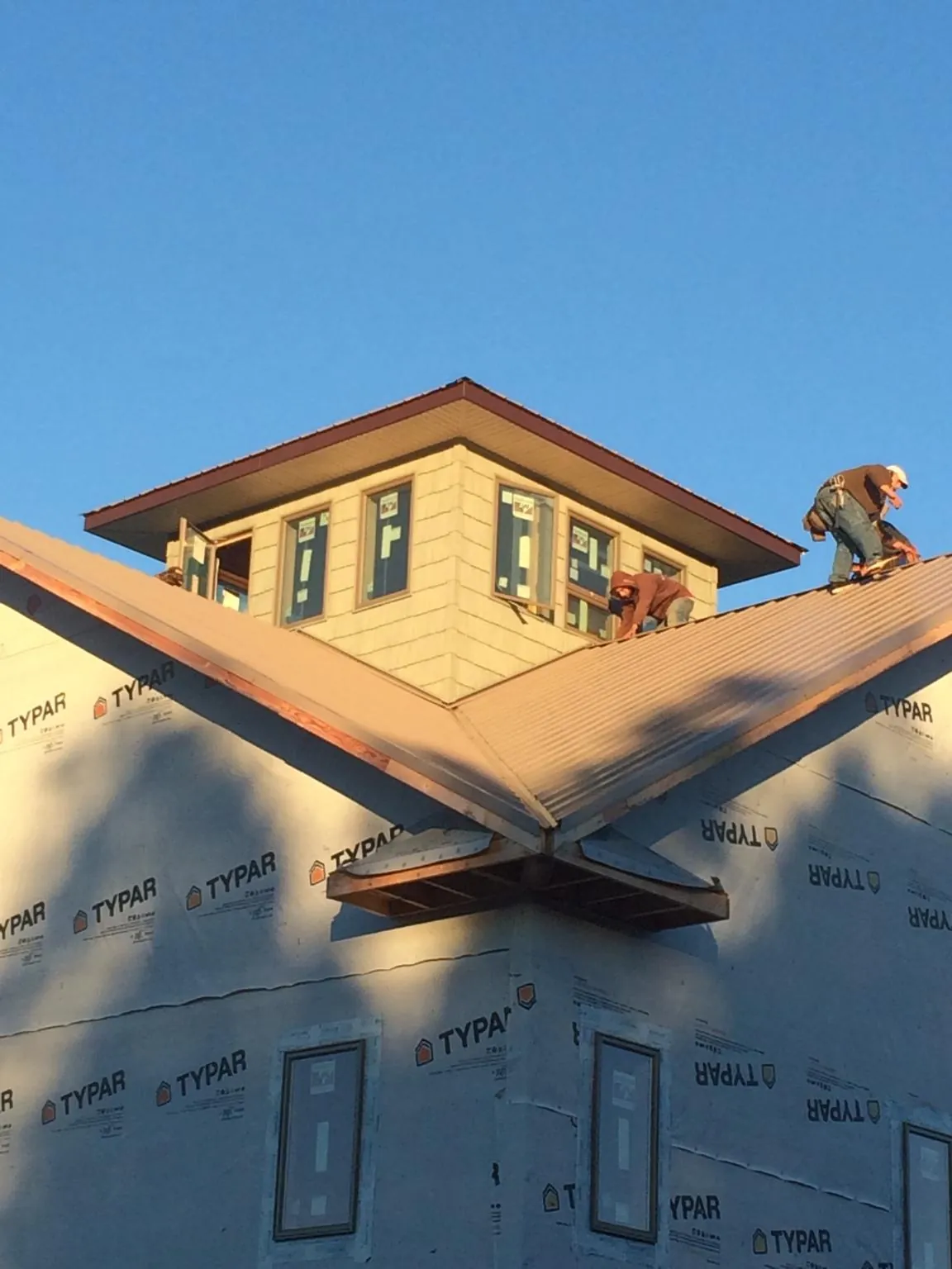 Roofers working around a rooftop cupola on a new metal roof at sunset — Roof Waterproofing in Trego by Roofing Brothers